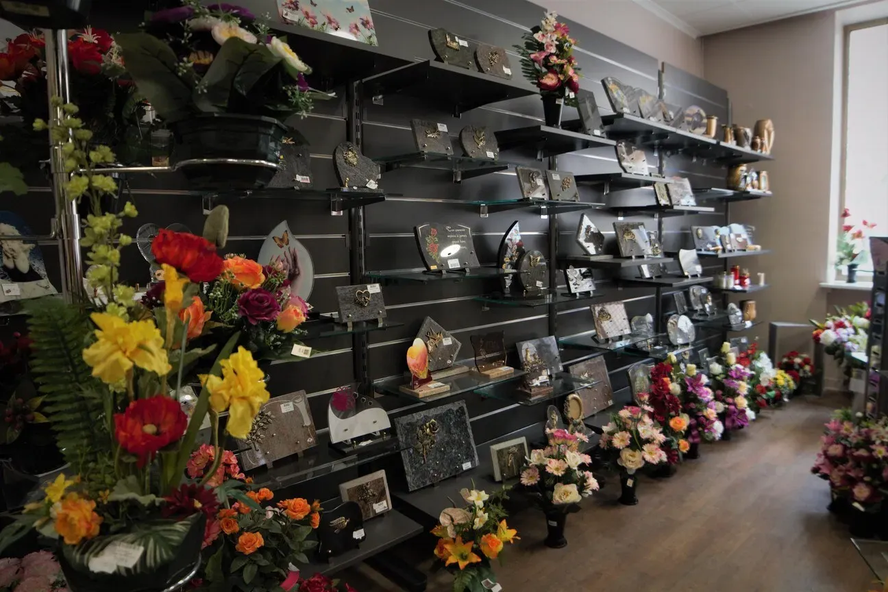 Rayonnages en magasin exposant des plaques funéraires et des fleurs artificielles.